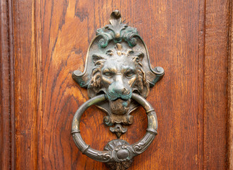Close-up of an old door knocker in oxidized copper in the shape of a lion's head and with a handle ring on a wooden door, Sestri Levante, Genoa, Liguria, Italy 