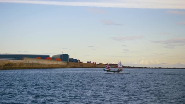 Small fishing boat sails into the port at Peterhead, Scotland, filmed from a yacht at sea.