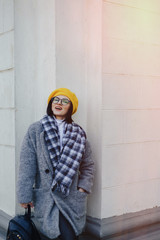 Attractive young girl in glasses in coat and yellow Beret on a simple light background