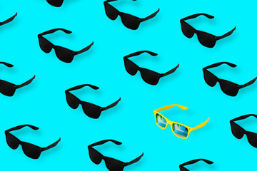 Black glasses on pastel blue background. Among the many black glasses alone yellow. Minimum summer...