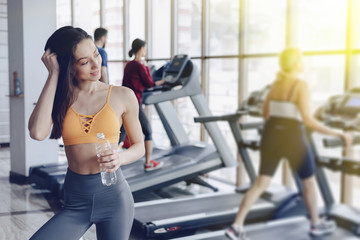 Fototapeta na wymiar young attractive girl in the gym drinking water on the background of treadmills