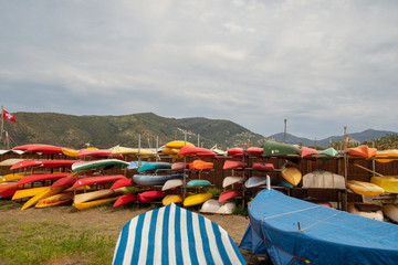 Scenic view of a storage of colorful kayaks, canoe and sup boards on the beach of the Bay of the Fairy Tales in Sestri Levante with covered rowing boats in the foreground in springtime, Liguria, Italy