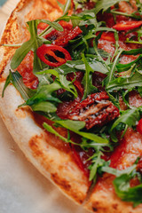 Neapolitan spicy pizza with ham, cheese, arugula, basil, tomatoes, pepperoni pepper sprayed with cheese on a wooden board on a tablecloth in a cell with a place for text