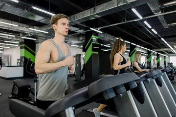 Fototapeta na wymiar Young active people exercising in the gym. Young attractive women and handsome man doing cardio training in gym