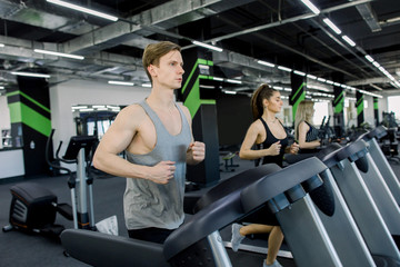 Fototapeta na wymiar Picture of people running on treadmill in gym. Handsome trainer and two young women on the treadmill in gym. Fitness concept