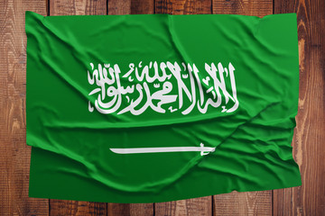 Flag of Saudi Arabia on a wooden table background. Wrinkled Saudi flag top view.