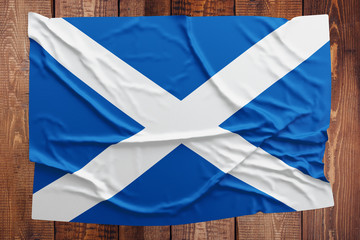 Flag of Scotland on a wooden table background. Wrinkled Scottish flag top view.