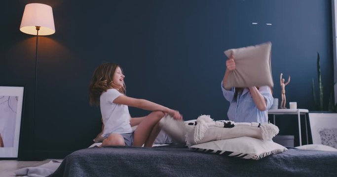 Mommy and kid daughter having pillow fight together, young babysitter nanny playing funny game with kid girl at home, happy mother and child enjoy spending time together, family leisure fun activity