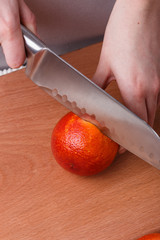 young woman in a gray apron cuts blood orange