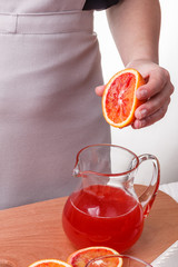 young woman in a gray apron squeezes juice of orange blood