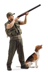 Male hunter aiming with a shotgun upwards with a beagle dog next to him