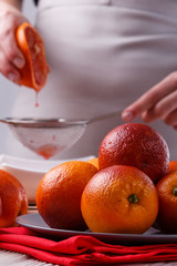 young woman in a gray apron squeezes juice of orange blood