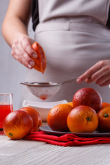 young woman in a gray apron squeezes juice of orange blood