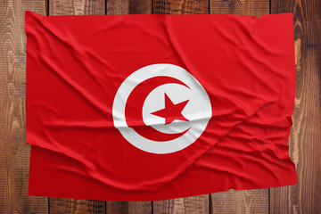 Flag of Tunisia on a wooden table background. Wrinkled Tunisian flag top view.
