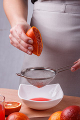 young woman in a gray apron squeezes juice of orange blood