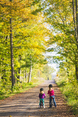 Obraz premium Two sisters ride bikes down a quiet country road; two children enjoy a fall bike ride