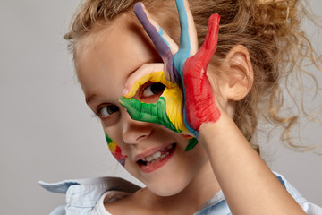 Beautiful little girl with a painted hands and cheeks is posing on a gray background.