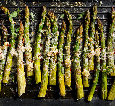 Grilled green asparagus with the addition of parmesan cheese, garlic and aromatic herbs on the grill plate, top view