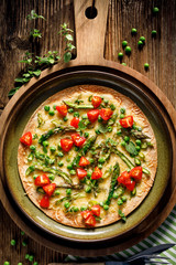 Tortilla Pizza with green asparagus, peas, cherry tomatoes, herbs and cheese, top view