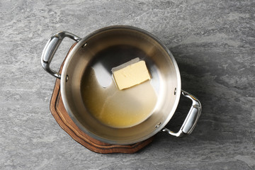 Pot with melting butter on grey background, top view
