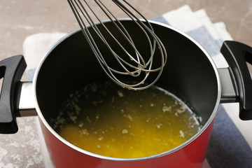 Pot with melting butter and whisk on table, closeup