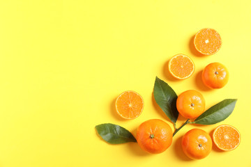 Fresh tangerines and leaves on color background, flat lay with space for text. Citrus fruits