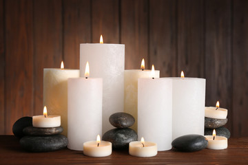 Beautiful composition with candles and stones on table against wooden background