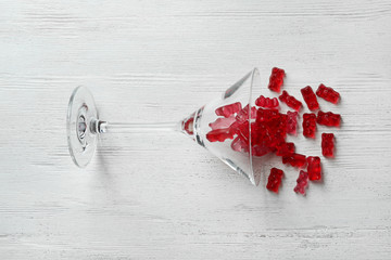 Martini glass with delicious jelly bears on wooden background, top view