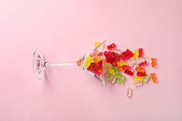 Martini glass with delicious color jelly bears on color background, top view