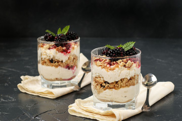 Curd dessert with blackberries and cookies in glass on a dark background