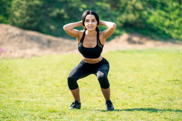 Slender beautiful girl with dark hair in a sports uniform crouches in nature, a symbol of healthy lifestyles, strong personality and desire for success and athletic body