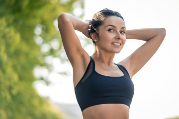 Fototapeta premium Slim beautiful girl with dark hair in a sports uniform is stretched in nature with a smile and look into the frame, a symbol of a healthy lifestyle and athletic body.