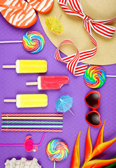 Obraz premium Summer vacation theme flatlay overhead with sunhat, lollipops, ice creams and sunglasses on purple background.