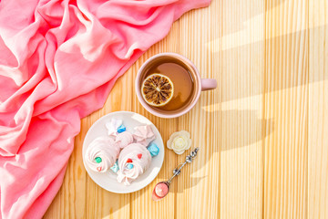 Romantic sweet breakfast concept. Green tea, lemon, meringue (cake). On wooden background with pink cloth, top view.
