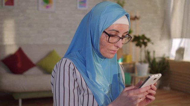 Portrait young muslim woman in hijab with a scar from a burn on her face uses a smartphone