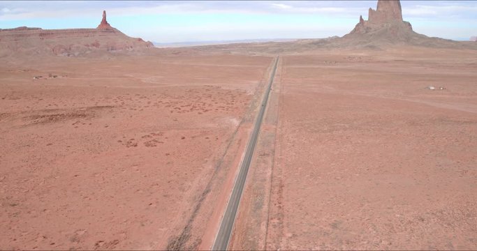 Aerial Pan Right: Cars Driving Down Road In Middle Of Desert Plain in Monument Valley, UT