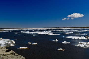 Calm flow of the river with ice floes during the spring thaw. View from the coastal dike.