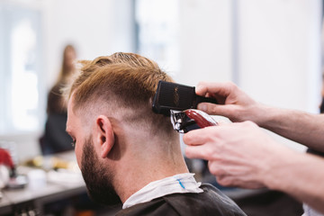 Close up shot of man getting trendy haircut at barber shop. Male hairstylist serving client, making haircut using machine and comb