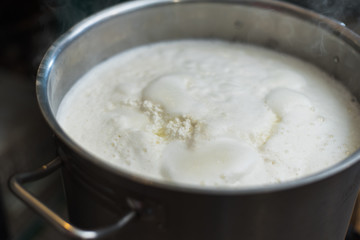 Cooking cottage cheese and cheese at home. Man creates cheese, heating milk and whey in an aluminum pan. Rustic homemade dairy products