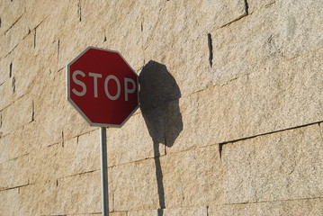 Sinal de stop junto de uma parede de pedra com sombra projectada, STOP