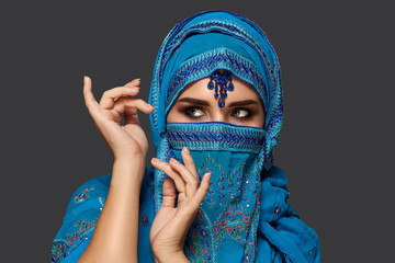 Studio shot of a young beautiful woman wearing the blue hijab decorated with sequins and jewelry. Arabic style.