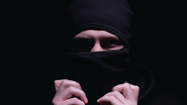 Serious man wearing balaclava preparing for terrorism action, black background