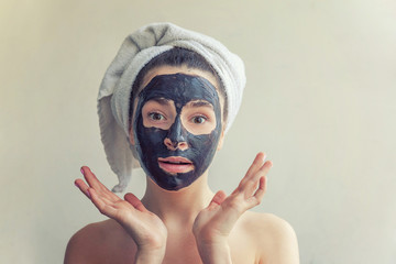 Beauty portrait of woman in towel on head applying black nourishing mask on face, white background isolated. Skincare cleansing eco organic cosmetic spa relax concept