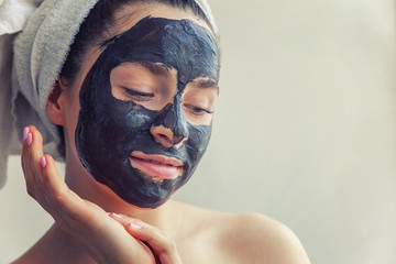 Beauty portrait of woman in towel on head applying black nourishing mask on face, white background isolated. Skincare cleansing eco organic cosmetic spa relax concept