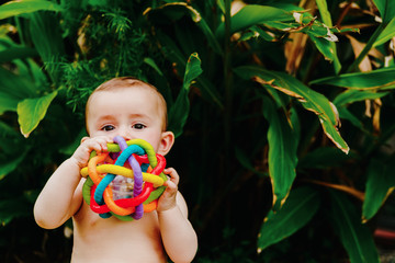 Baby sitting on the barefoot grass nibbling on a plastic toy.
