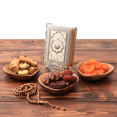 Ramadan iftar party concept. Islamic holy book Quran and rosary beads with delicious dates, dried figs, dried apricots on bamboo plates and lantern on a pine wooden table background. Ramadan Kareem