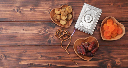 Ramadan iftar party concept. Islamic holy book Quran and rosary beads with delicious dates, dried figs, dried apricots on bamboo plates and lantern on a pine wooden table background. Ramadan Kareem