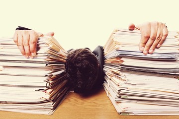 Tired young businessman with stack of papers and laptop