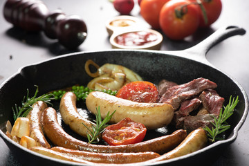 studio shot of grilled sausages with lettuce and tomato ketchup on black background