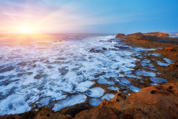 The stony coast of the Atlantic Ocean is washed by the waves during sunset, Essaouira
